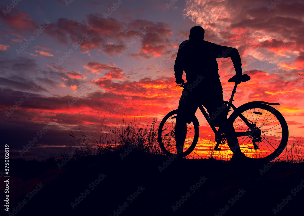 Obraz premium cyclist with a bicycle, in the background fiery sunset.
