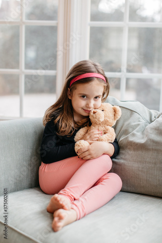 Beautiful young girl sitting on a big chair with her teddy bear photo