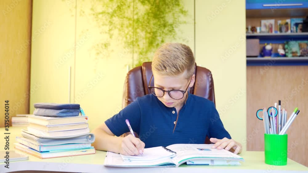 cute blond teenager. Child Little Boy Kid schoolboy in glasses learning writing homework in room home, studying making notes sitting at table. Elementary education, children, people, school concept cute blond teenager. Child Little Boy Kid schoolboy in glasses learning writing homework in room home, studying making notes sitting at table. Elementary education, children, people, school concept