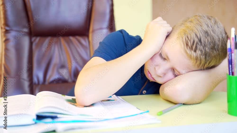 close-up portrait of a young cute boy, schoolboy lying at the table closes his eyes and falls asleep teaches lessons. studies homework sad and exhausted put head on book. teenager sleeps on notebooks close-up portrait of a young cute boy, schoolboy lying at the table closes his eyes and falls asleep teaches lessons. studies homework sad and exhausted put head on book. teenager sleeps on notebooks