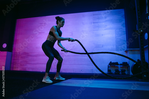 Sweaty athlete woman training hard in dark, moody gym.