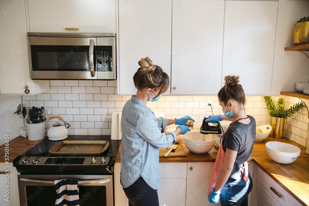 Mom and daughter baking cookies wearing face mask and gloves. Mom and daughter baking cookies wearing face mask and gloves.