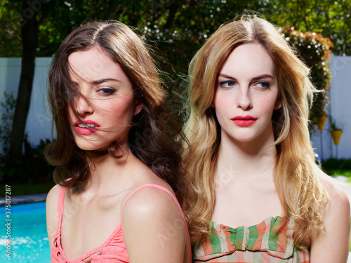 Closeup portrait of two women in vintage style bathing suits, sitting outside by a pool. photo