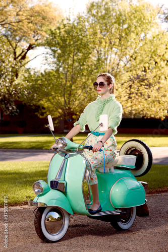 Contemporary vintage inspired shot of a woman riding a Vespa on a sunny afternoon with sunglasses on.  photo