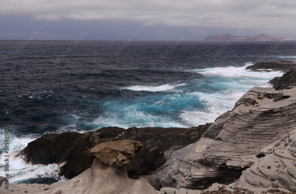 North coast of Gran Canaria, Canary Islands, Banaderos area, waves are breaking against elevated rock 
with salt evaporation ponds Salinas de Bufadero