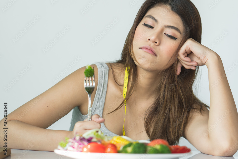 unhappy asian women is on dieting time looking at broccoli on the fork. girl do not want to eat vegetables and dislike taste of broccoli. unhappy asian women is on dieting time looking at broccoli on the fork. girl do not want to eat vegetables and dislike taste of broccoli.