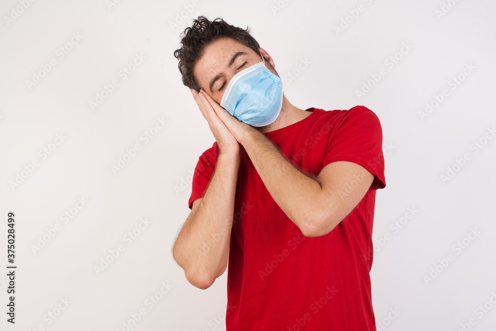 Young caucasian man with short hair wearing medical mask standing over isolated white background sleeping tired dreaming and posing with hands together while smiling with closed eyes.