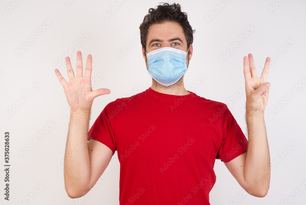 Young caucasian man with short hair wearing medical mask standing over isolated white background showing and pointing up with fingers number eight while smiling confident and happy. Young caucasian man with short hair wearing medical mask standing over isolated white background showing and pointing up with fingers number eight while smiling confident and happy.