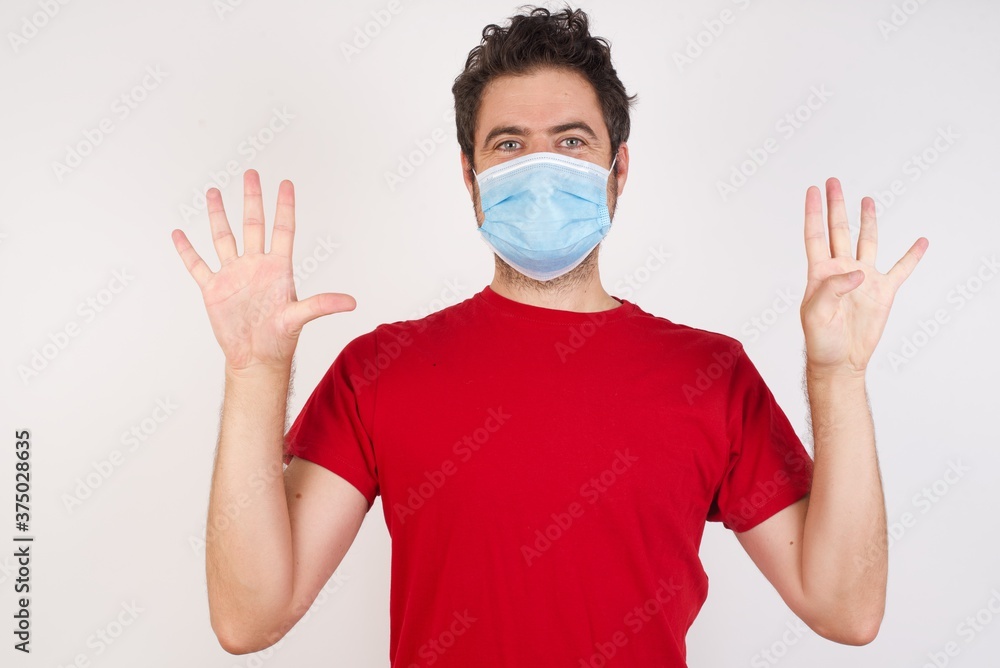 Young caucasian man with short hair wearing medical mask standing over isolated white background showing and pointing up with fingers number nine while smiling confident and happy. Young caucasian man with short hair wearing medical mask standing over isolated white background showing and pointing up with fingers number nine while smiling confident and happy.