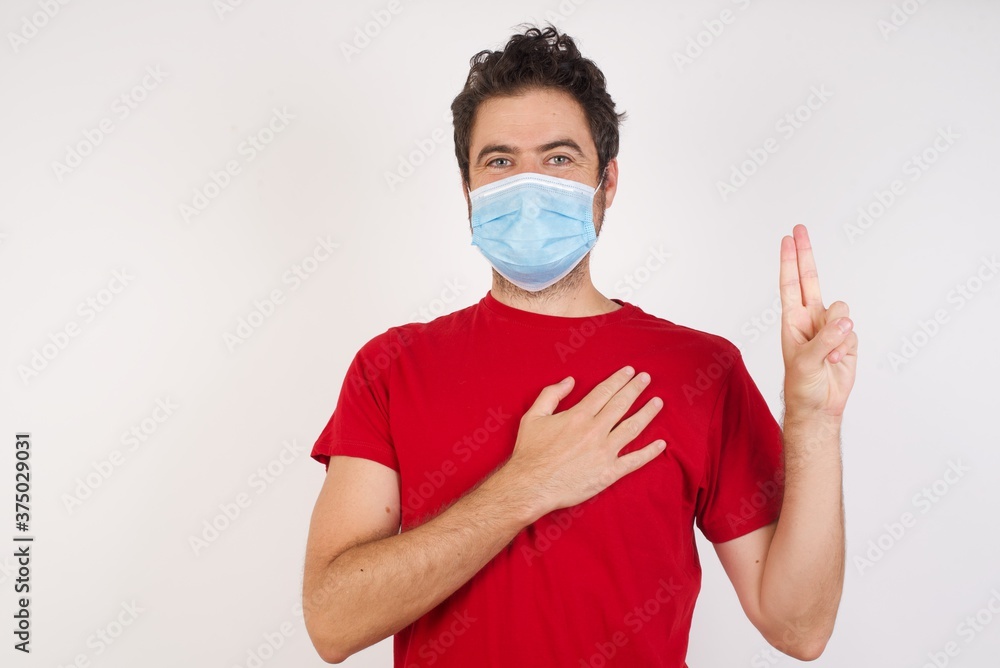 Young caucasian man with short hair wearing medical mask standing over isolated white background smiling swearing with hand on chest and fingers up, making a loyalty promise oath. Young caucasian man with short hair wearing medical mask standing over isolated white background smiling swearing with hand on chest and fingers up, making a loyalty promise oath.