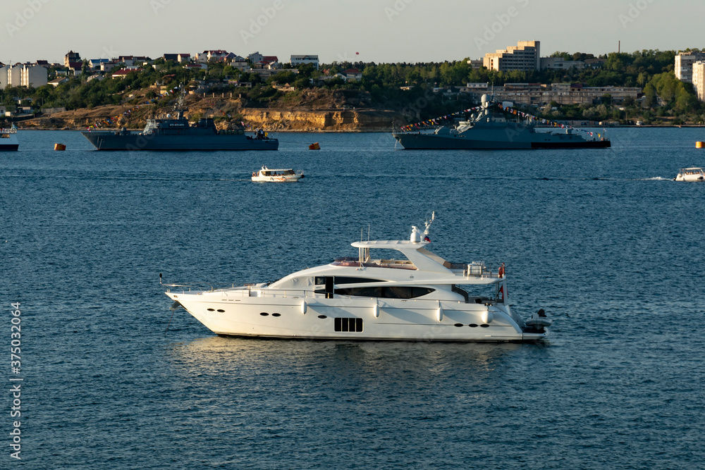 Fototapeta premium White motor yacht in the seaport against the backdrop of warships.