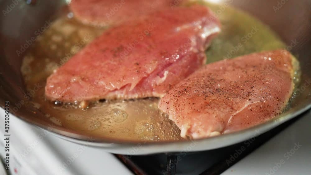 Boneless, skinless chicken breasts seasoned and sizzling in oil in a skillet on the stove - slow motion Boneless, skinless chicken breasts seasoned and sizzling in oil in a skillet on the stove - slow motion