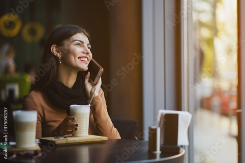 brunette girl using her phone while drinking coffee at a restaurant