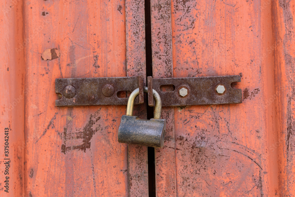 Padlock on metal gate hinges. old orange paint with a red tint, rust. Closed door concept. Padlock on metal gate hinges. old orange paint with a red tint, rust. Closed door concept.