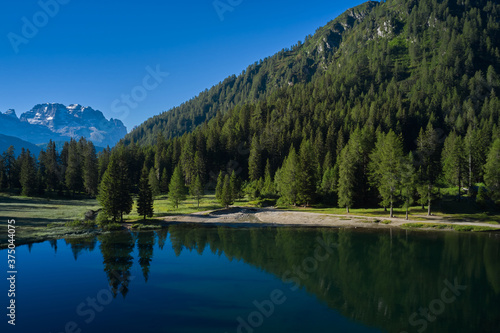 Reflections in water. Sun on a crystal blue sky. Reflections of trees, mountains, sky in a mountain lake. Early morning in the Alps. Aerial view.