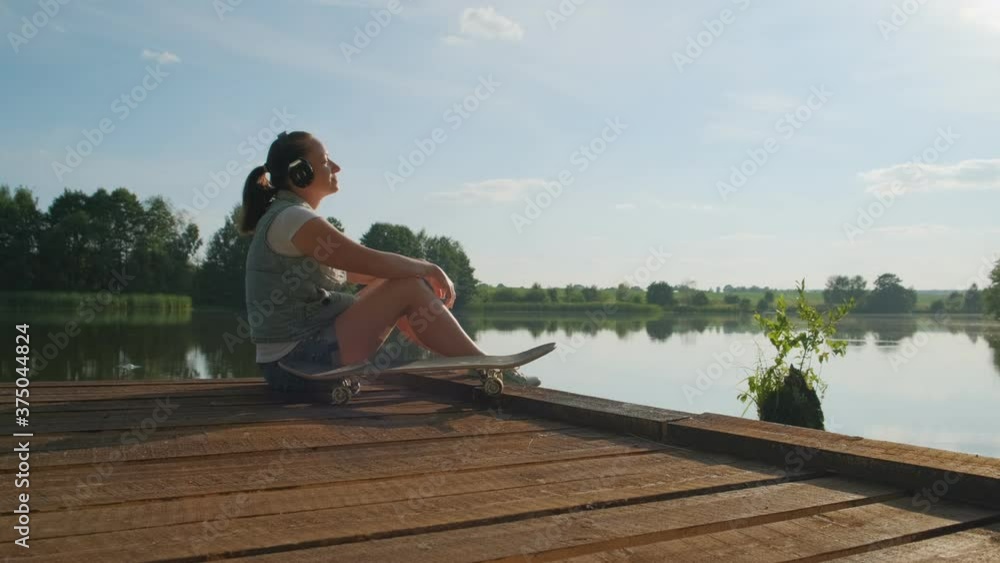 woman in headphones enjoys music and nature sitting on edge of wooden pier on lake. woman in headphones enjoys music and nature sitting on edge of wooden pier on lake.