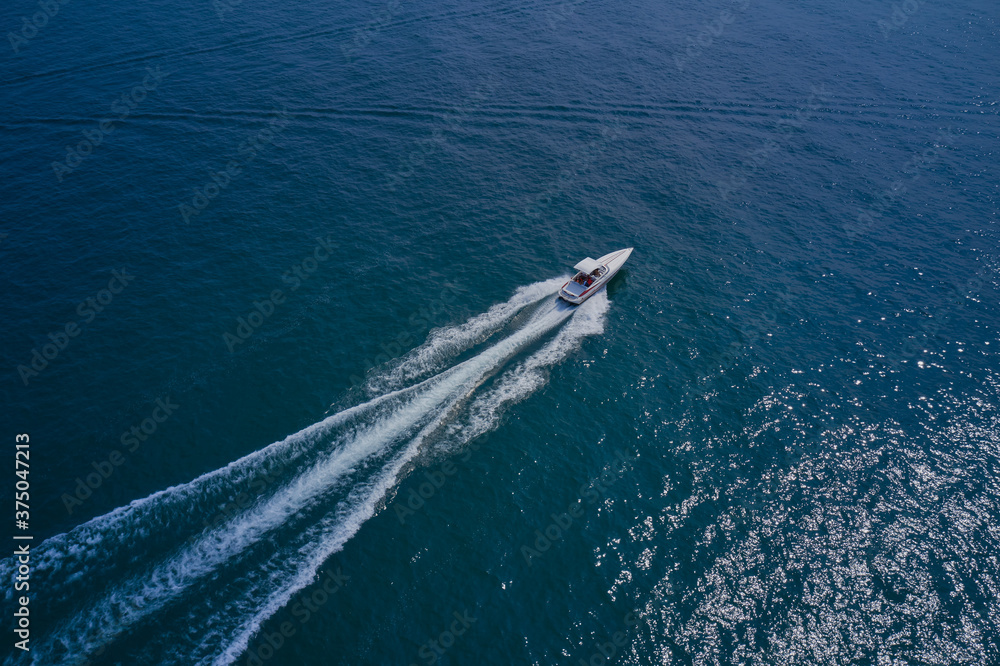 Drone view of a yacht sailing across the blue clear waters. Top view of a white yacht sailing in the blue sea. Aerial view luxury motor yacht.