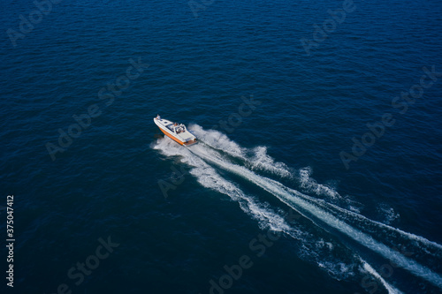 Top view of a white boat sailing in the blue sea. A boat with a motor on blue water. Aerial view luxury motor boat.  Top view of the boat. © Berg