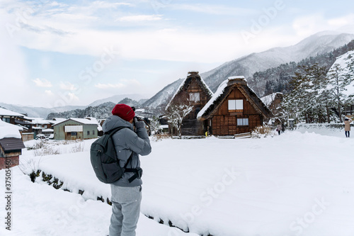 Young Man traveller taking a photo of Gassho-Zukuri houses at Shirakawa-go villages in snowfall day, view point in snowing fall winter, inscribed UNESCO World Heritage photo