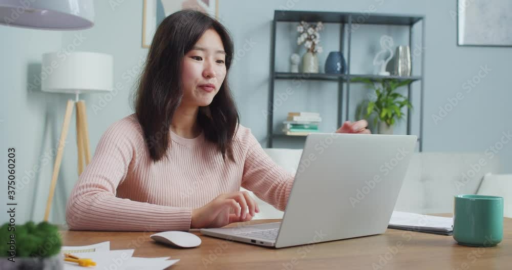 Pretty Asian woman sitting at table and talking to friend, family via video webcam chat. Chatty young girl using laptop to call through Internet at home. Communication, social media concept. Pretty Asian woman sitting at table and talking to friend, family via video webcam chat. Chatty young girl using laptop to call through Internet at home. Communication, social media concept.