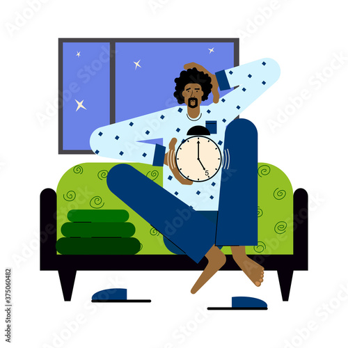 A tired man sits in bed early in the morning with an alarm clock in his hands.