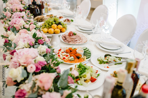 The composition of purple, pink flowers and greenery standing on served table in the area of wedding party. Table newlyweds served with dishes and cutlery. Close up.