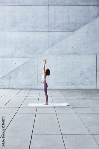 Frau/Mädchen in Pastell gekleidet macht Outdoor Yoga Übungen/Sonnegruß in moderner Beton Architektur. Urbanes Leben. 
