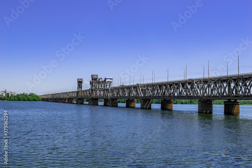 Metal Amur bridge over the Dnieper river in Dnipro (Ukraine), side view. Modern monument of engineering art against the background of a blue water surface. Background with copy space