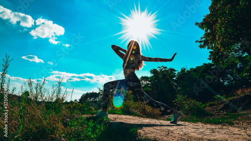 Woman Doing Yoga On Mountain Against Sky and Sun. Hard light. Silhouette of girl doing outdoor sport stretch. photo