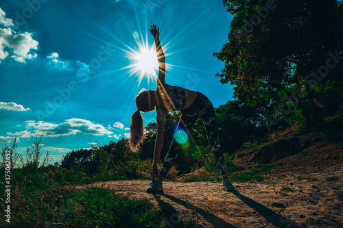 Woman Doing Yoga On Mountain Against Sky and Sun. Hard light. Silhouette of girl doing outdoor sport stretch. photo