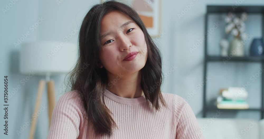 Portrait of charming beautiful girl sitting at table in modern room with minimalist interior at home. Close up of pretty young Asian woman looking at camera and smiling. Indoors face shoot. Portrait of charming beautiful girl sitting at table in modern room with minimalist interior at home. Close up of pretty young Asian woman looking at camera and smiling. Indoors face shoot.