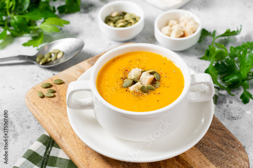 Pumpkin soup. Pumpkin cream soup in a white plate on the light gray kitchen table. Vegetarian autumn soup close up