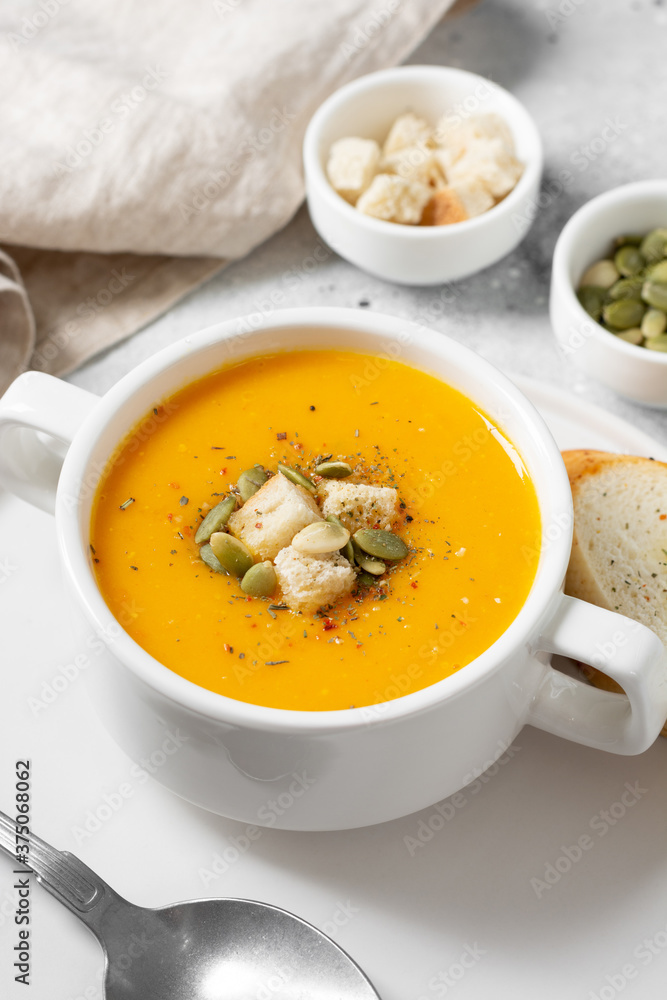 Pumpkin soup. Pumpkin cream soup in a white plate on the light gray kitchen table. Vegetarian autumn soup closeup Pumpkin soup. Pumpkin cream soup in a white plate on the light gray kitchen table. Vegetarian autumn soup closeup