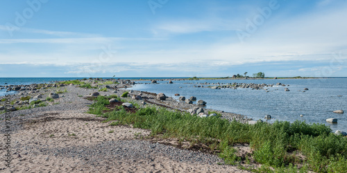 Sand path leading to a rocky peninsula. The trail passes through flowering rose hips and leads to the Baltic Sea. Estonia. Baltic.