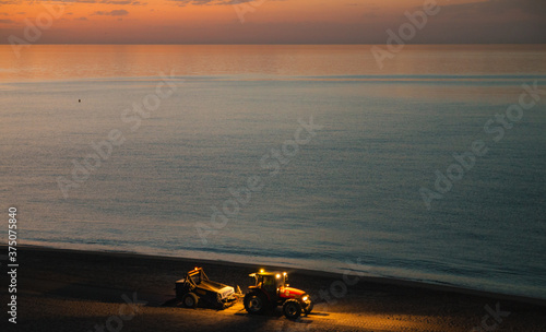 Beach before sunrise with a tractor cleaning up the beach. photo