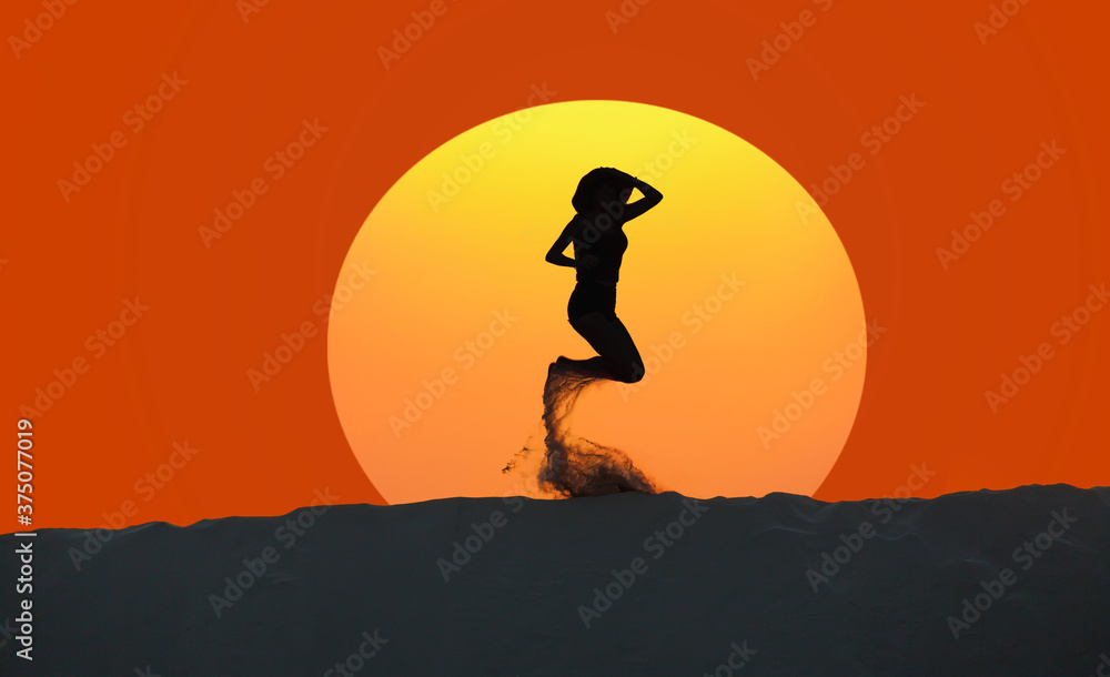 Silhouette of beautiful girl jumping on the desert at amazing sunset sand dune in the background 