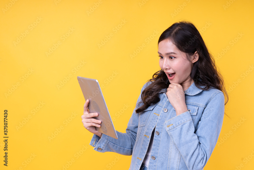 Beautiful Asian women are excited and amazed on the orange background. A woman sees a sale on an online shopping site on a tablet screen. Beautiful Asian women are excited and amazed on the orange background. A woman sees a sale on an online shopping site on a tablet screen.