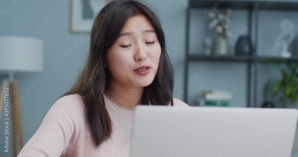 Charming Asian woman sitting at table and using laptop in modern room with minimalist interior. Joyful young girl talking to family, friends via video, webcam chat. Social media, Internet. Charming Asian woman sitting at table and using laptop in modern room with minimalist interior. Joyful young girl talking to family, friends via video, webcam chat. Social media, Internet.