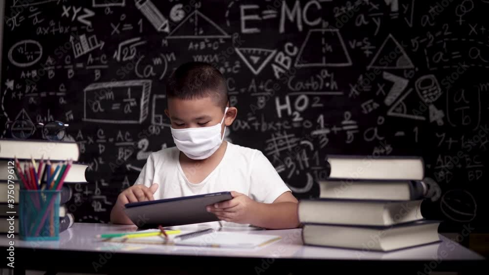 Asian boy with face mask thinking while using smart pad for digital learning at home. New normal education concept. 4K Asian boy with face mask thinking while using smart pad for digital learning at home. New normal education concept. 4K