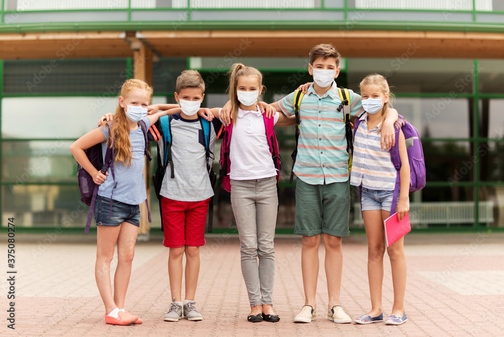 education, childhood and pandemic concept - group of elementary school students wearing face protective medical mask for protection from virus disease hugging outdoors