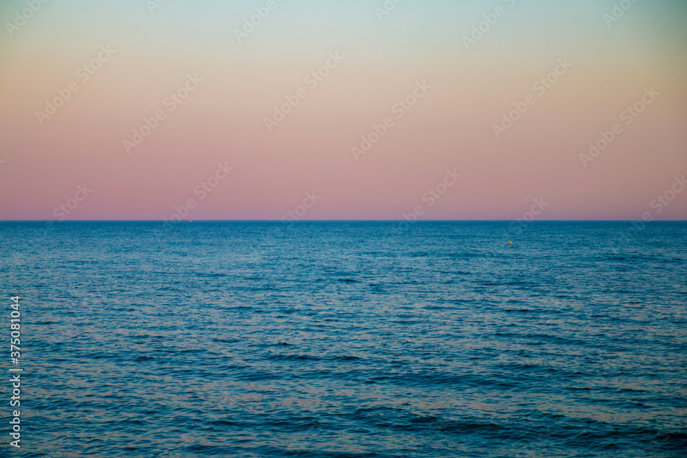A scenic view with blue sea and colorful sky after sunset in Spain