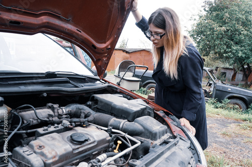 the girl looks under the hood of the car
