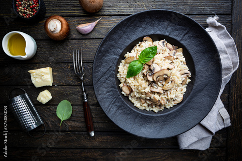 Risotto with mushrooms in a black plate over rustic wooden background, top view