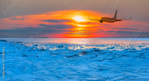 Airplane in the sky at sunset - Beautiful landscape cracking ice  frozen sea coast at sunrise 