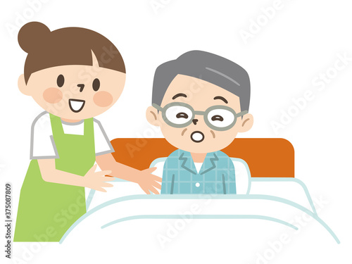 ベッドで寝るシニア男性を介助する若い介護士