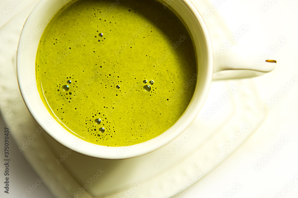 Japanese matcha green tea is poured into a white mug and on a white saucer in powder. Tea set on a textured napkin. Invigorating drink in a cafe, cooking, cheerfulness, antioxidant. space for text Japanese matcha green tea is poured into a white mug and on a white saucer in powder. Tea set on a textured napkin. Invigorating drink in a cafe, cooking, cheerfulness, antioxidant. space for text
