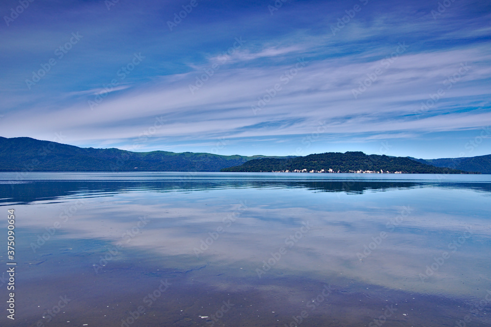 青空を湖面に映す湖。屈斜路湖、北海道。
A landscape of a lake that reflects the blue sky with thin clouds on the surface of the lake. Lake Kussharo, Hokkaido, Japan.