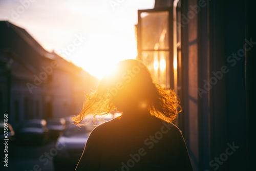 Silhouette of a woman with hair in the rays of the setting sun on the street during sunset