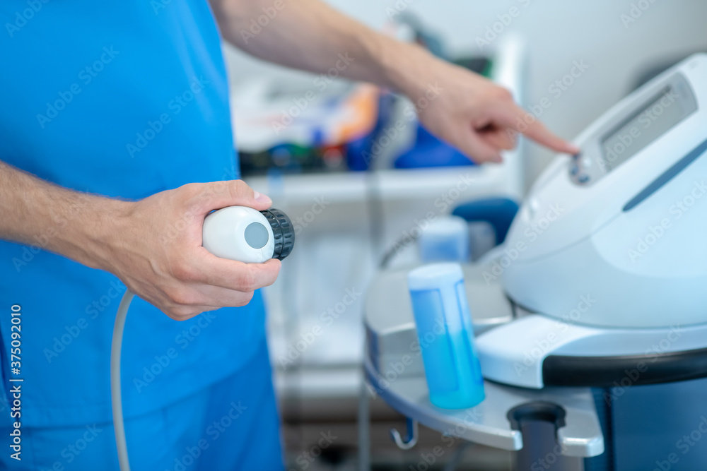 Obraz premium Close-up of male hands pressing buttons on physiotherapy ultrasound machine