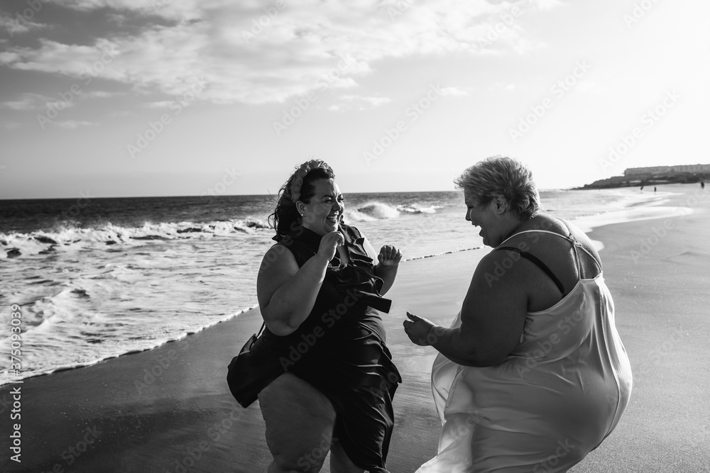 © DisobeyArt - Plus size women dancing on the beach having fun during summer vacation - Happy curvy female laughing together - Overweight body and happiness concept - Black and white editing